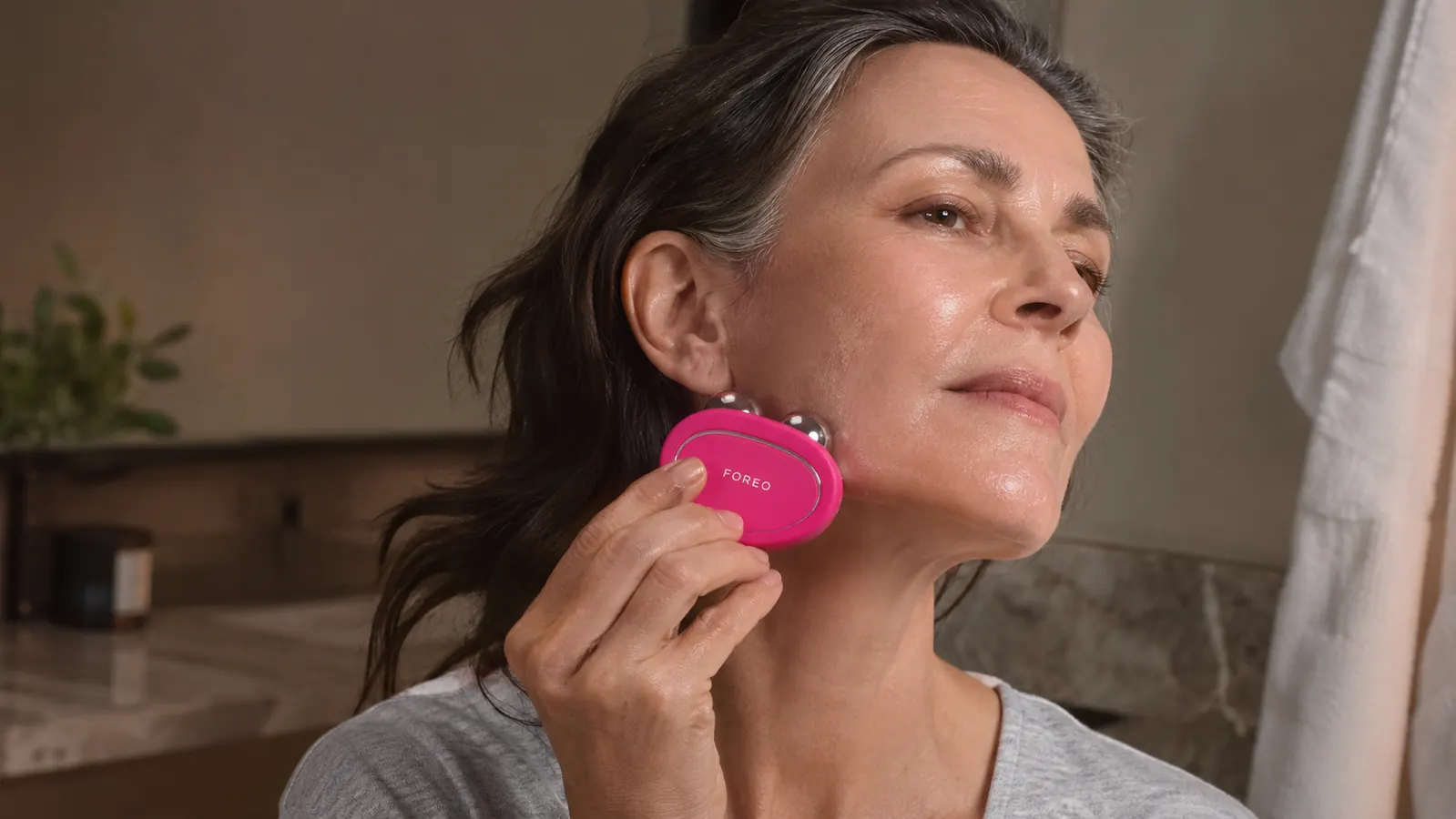 Close-up of a hand holding a FOREO Bear microcurrent device against the jawline, sweeping upward toward the ear